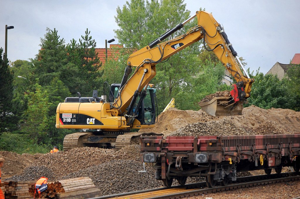Ein CAT 319D LVA der Baufirma STRABAG entl�dt einen Drehgestellflachwagen mit altem Gleisschotter, Baustelle am Bhf. Flughafen Berlin-Sch�nefeld, 18.08.10 