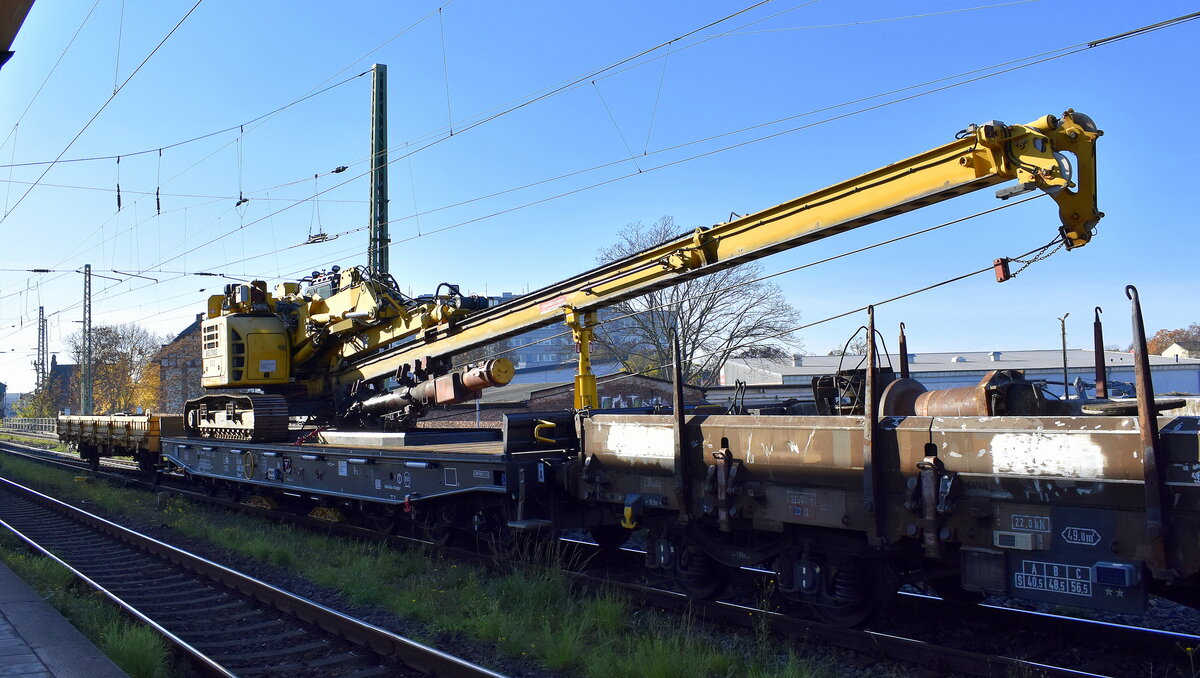 Drehgestell-Flachwagen der DB Cargo im Einsatz für die DB Bahnbau Gruppe mit der Nr. 31 80 D-DB 4865 573-8 Samms 709 mit Außenbeleuchtung u. Kettenbohrramme Delmag G42B beladen + Beiwagen am Haken von PRESS  204 271-1  am 06.11.25 Höhe Bahnhof Magdeburg-Neustadt.