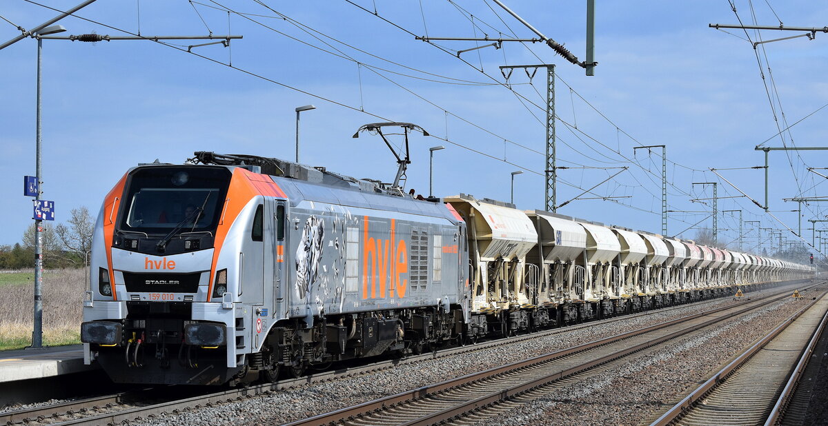 Havelländische Eisenbahn AG, Berlin-Spandau [D] mit ihrer Eurodual Lok  159 010  [NVR-Nummer: 90 80 2159 010-8 D-HVLE] und einem Schüttgutwagenzug mit Sand am 09.04.25 Höhe Bahnhof Rodleben.