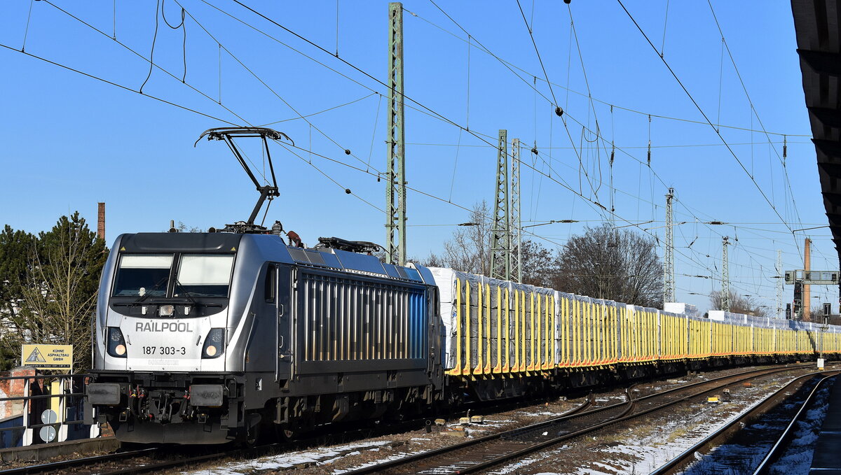 SETG - Salzburger Eisenbahn TransportLogistik GmbH, Salzburg [A] mit der geleasten Railpool Lok  187 303-3  [NVR-Nummer: 91 80 6187 303-3 D-Rpool] und einem Ganzzug TRANSWAGFGON Drehgestell-Rungenwagen gemietet von der Mercer Timber Products GmbH mit Holzprodukten in Folie am 19.02.25 Höhe Bahnhof Magdeburg-Neustadt.