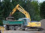 HKL Leasingbaumaschine, ein NEW HOLLAND KOBELCO E215B Raupenbagger schaufelt Gleisschotter in einen Baukipper, 02.09.10 Baustelle am Bhf.